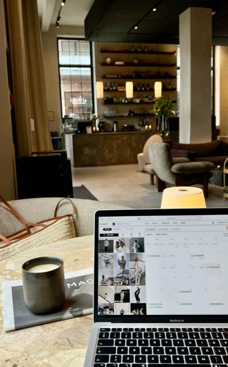 A laptop, candle, and coffee mug on a marble table in a softly lit cafe lounge